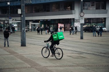 KATOWICE. POLAND - 26 Mart 2021: hızlı restoran teslimatı için bisikletli ya da motosikletli adam. Paket servisi için yemek paketi. Uber yemek dağıtırken mobiletle kurye yiyor.