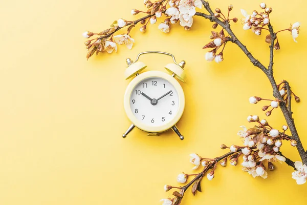 春の背景テーブル 黄色の目覚まし時計と5月の花や4月の花の性質 バナーのために 背景に桜の花の枝 コピースペースと夢のようなロマンチックな画像 — ストック写真