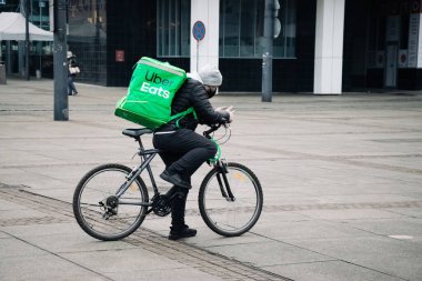 KATOWICE. POLAND - 26 Mart 2021: hızlı restoran teslimatı için bisikletli ya da motosikletli adam. Paket servisi için yemek paketi. Uber yemek dağıtırken mobiletle kurye yiyor.