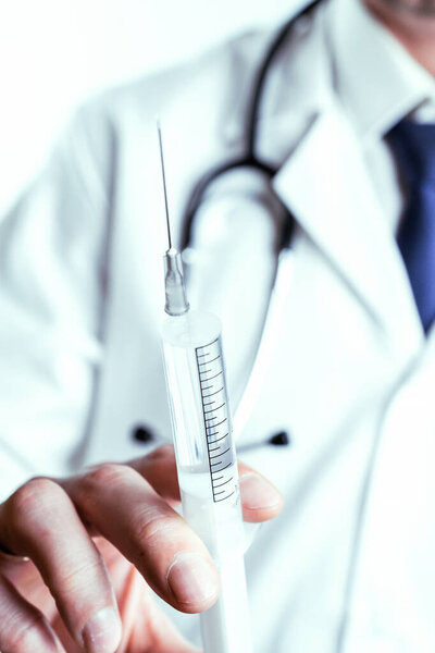 Vaccine dose medical injection. Selective focus, hospital white doctor gown, stethoscope. Nurse hand in blue gloves holding syringe with needle. Liquid drug or narcotic. Health care in hospital