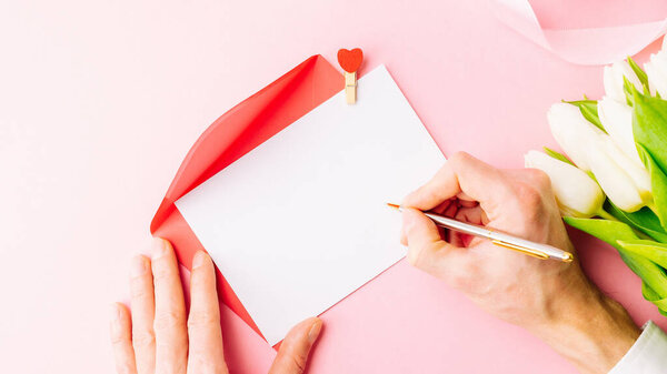 Mothers day background. Spring white tulip flower, gift box with red ribbon on flat lay pink background. Top view wedding love minimal concept