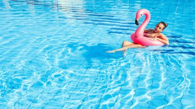 Yaz zamanı. Mavi havuz suyunda rahatlayan pembe şişme flamingolu bikinili mutlu genç seksi kız. Havuz suyu yüzmek, eğlenmek ve seyahatin tadını çıkarmak.