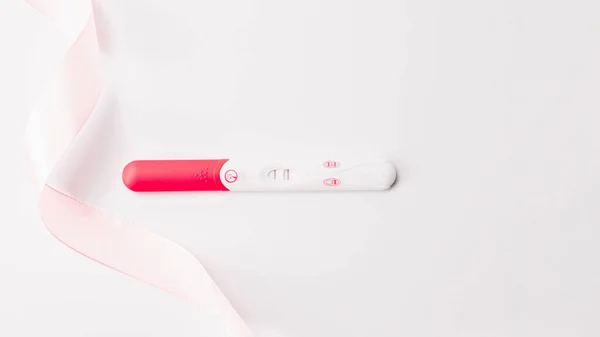 陽性の妊娠検査結果。白い背景にピンクのシルクリボンで女性妊娠検査。医療保健婦人科、妊娠不妊妊産婦の概念. — ストック写真
