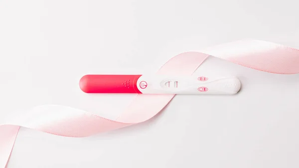 Risultato positivo del test di gravidanza. Test di gravidanza donna con nastro di seta rosa su sfondo bianco. Sanità medica ginecologica, gravidanza fertilità maternità concetto di persone. — Foto Stock