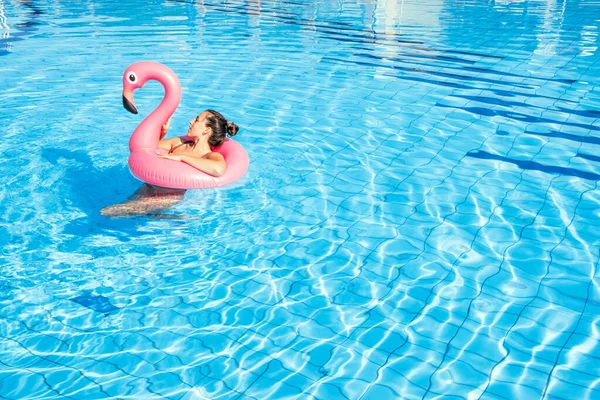 Женщина за бассейном. Счастливая молодая сексуальная девушка в купальнике с розовым фламинго плавает в голубой воде. Путешествия с роскошным образом жизни. — стоковое фото