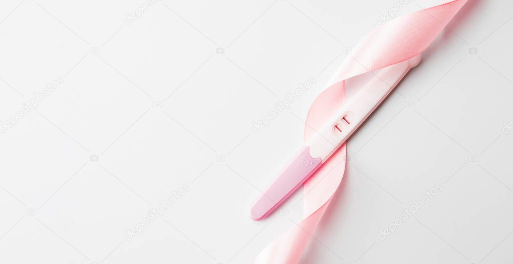 Positive pregnancy test result. Woman pregnant test with pink silk ribbon on white background. Medical healthcare gynecological, pregnancy fertility maternity people concept