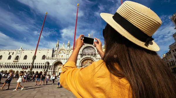 Travel blogger Venice italy. Photographer girl with smartphone in Venice San Marco square. Paint building house in travel Europe Venezia city. Hispter tourist using her phone outdoors