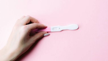 Hamilelik testi kiti. Kadın eli, pembe arka planda ipek kurdeleyle pozitif hamilelik testi yapıyor. Tıbbi sağlık, jinekoloji, gebelik, doğurganlık, doğum ve doğum insanları kavramı