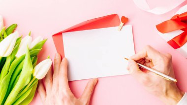 Anneler Günü geçmişi. Bahar beyazı lale çiçeği, üzerinde kırmızı kurdele olan hediye kutusu pembe arka planda yatıyordu. Üst görünüm düğün aşkı minimum konsept