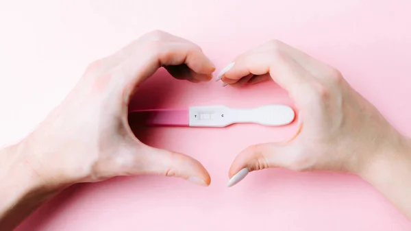 妊娠検査のカップル ピンクの背景にピンクのシルクリボンで手の中に肯定的な女性妊娠検査 新しい人生と新しい家族 出産管理の概念 — ストック写真