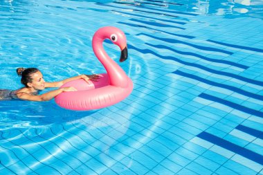 Yaz zamanı. Mavi havuz suyunda rahatlayan pembe şişme flamingolu bikinili mutlu genç seksi kız. Havuz suyu yüzmek, eğlenmek ve seyahatin tadını çıkarmak.