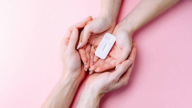 Hamilelik testi kiti. Kadın eli, pembe pankartta ipek kurdeleyle pozitif hamilelik testi yapıyor. Tıbbi sağlık, jinekoloji, gebelik, doğurganlık, doğum ve doğum insanları kavramı