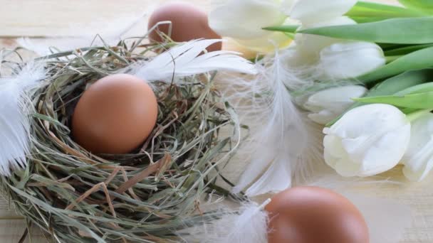 篮子的东方装饰 篮子里有天然彩蛋 带有春天郁金香 木制桌子背景上有白色羽毛 恭喜你的复活节设计 — 图库视频影像