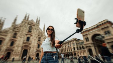 Seyahat blogcusu Milan Italya. Milan Piazza del Duomo 'da akıllı telefonu olan fotoğrafçı kız. Avrupa 'da Milano şehrinde boyama evi. Telefonunu açık havada kullanan bir turist.
