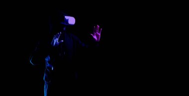 Sanal gerçeklik oyunu. Sanal gerçeklik teknolojisi için dijital gözlüklü genç adam karanlık neon arka planda izole edildi. 3 boyutlu simülasyonda çalışma ve sanal dünya