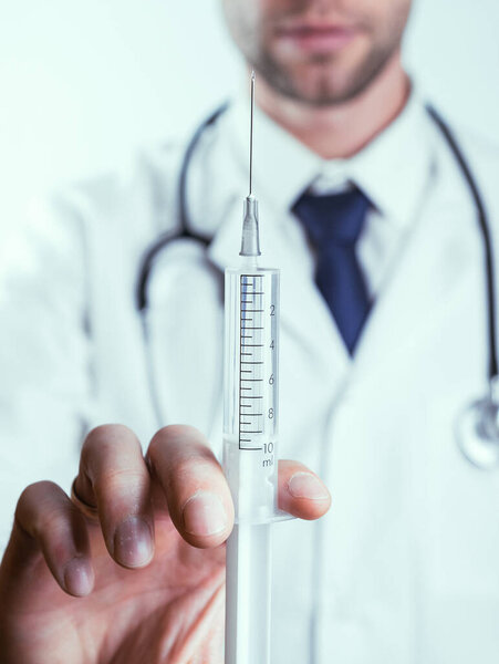 Syringe needle medical injection. Selective focus, doctor hand in blue gloves holding syringe with needle. Hospital white doctor gown, stethoscope. Syringe with flu vaccine with copy space