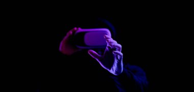 Sanal gerçeklik oyunu. Sanal gerçeklik teknolojisi için dijital gözlüklü genç adam karanlık neon arka planda izole edildi. 3 boyutlu simülasyonda çalışma ve sanal dünya