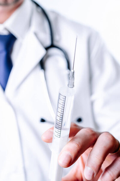 Syringe needle medical injection. Selective focus, doctor hand in blue gloves holding syringe with needle. Hospital white doctor gown, stethoscope. Syringe with flu vaccine with copy space.