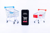 Internetové nakupování. Digitální smartphone s aplikací online obchodu, nákupní vozík na bílém pozadí. Jednoduchý internetový obchod. Koncept zkušenosti zákazníka