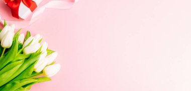 Anneler günü hediyesi. Bahar beyazı lale çiçeği, pembe arka planda kırmızı kurdeleli hediye. Sevgililer günü, doğum günü, kadınlar veya düğün günü konsepti