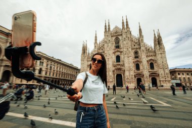 Seyahat blogcusu Milan Italya. Milan Piazza del Duomo 'da akıllı telefonu olan fotoğrafçı kız. Avrupa 'da Milano şehrinde boyama evi. Telefonunu açık havada kullanan bir turist.