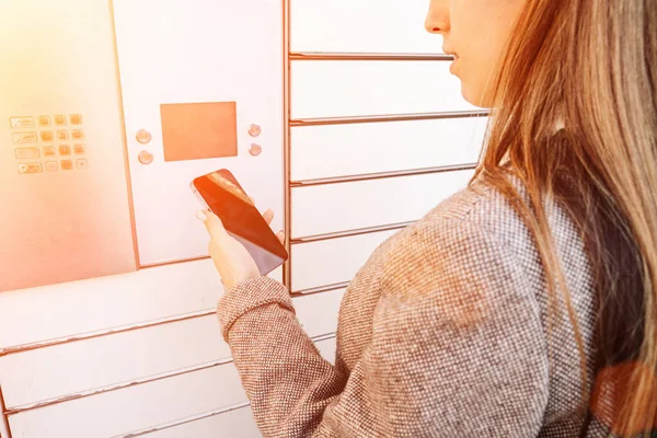 Pickup parcel. Courier box in woman hands at post delivery automat terminal. Self service post terminal and parcel delivery concept