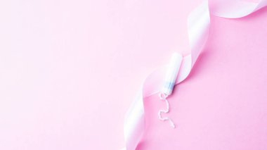 Adet öncesi tampon, kadın hijyeni. Pembe arka planda adet tamponu olan pembe kurdele. Adet dönemi kadınsı. Hijyen konsepti. Sağlık sigortası jinekolojik afişi
