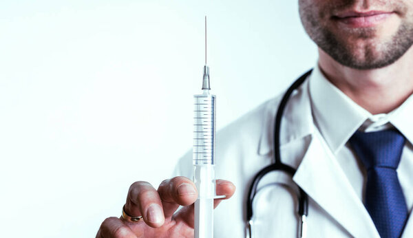 Syringe needle medical injection. Selective focus, doctor hand in blue gloves holding syringe with needle. Hospital white doctor gown, stethoscope. Syringe with flu vaccine with copy space