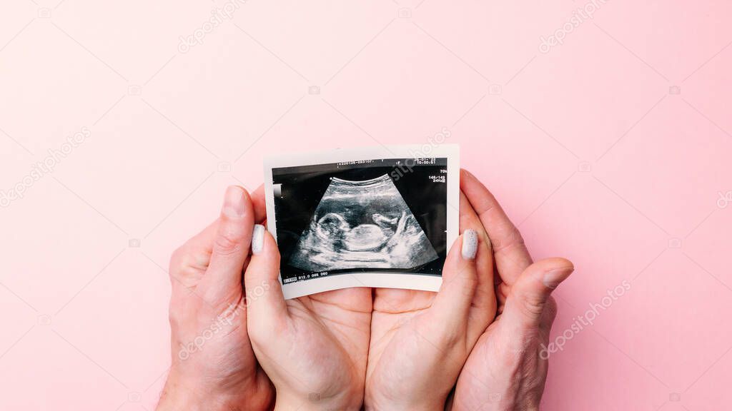 Ultrasound image pregnant baby photo. Woman hands holding ultrasound pregnancy picture on pink background. Pregnancy, medicine, pharmaceutics, health care and people concept
