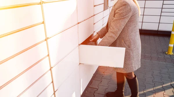 Automated locker. Parcel courier box in woman hands at post delivery automat terminal. Courier Puts Cardboard Package Into Parcel Locker