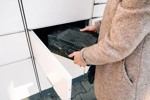 Pickup parcel. Courier box in woman hands at post delivery automat terminal. Self service post terminal and parcel delivery concept