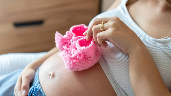 妊娠中の靴の赤ちゃん 妊婦の女の子は赤ん坊のための小さい子供の靴を保持する 妊娠出産をコンセプトとしています 美しい母親待っていますの赤ちゃん — ストック写真