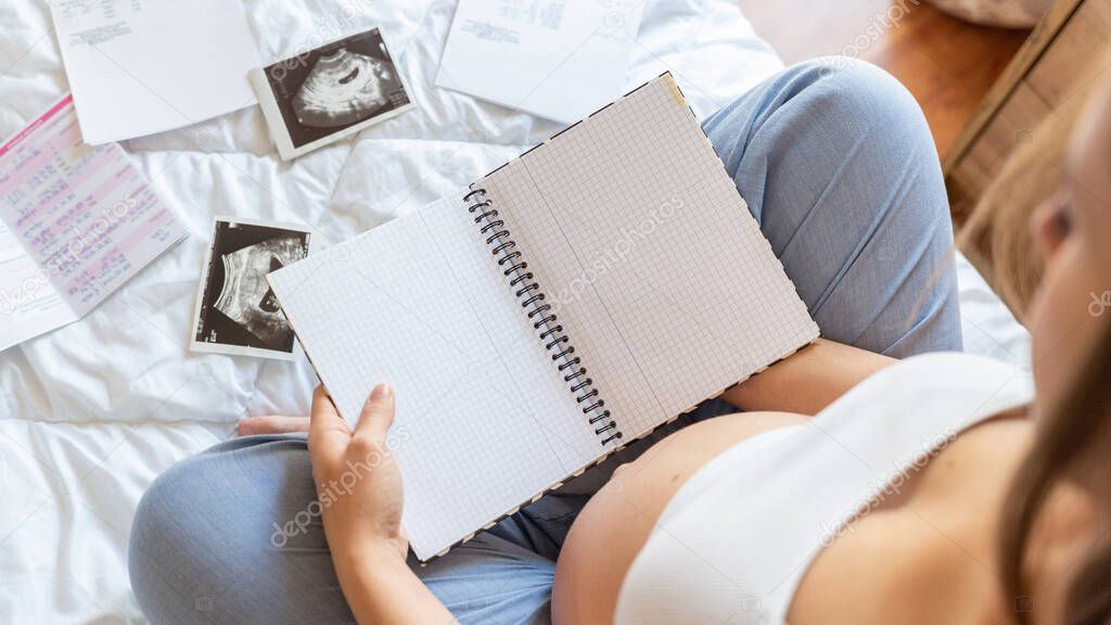 Baby list pregnant woman. Young pregnancy mother holding notepad. Pregnant lady writing check list of baby. Concept of maternity, expectation