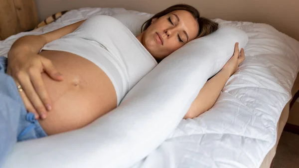 Pregnant pillow woman sleeping. Young pregnancy mother sleep with pregnant belly support pillow. Concept maternity, pregnancy, childbirth. Beautiful mother waiting of baby