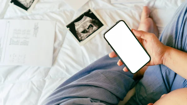Pregnancy smartphone screen. Pregnant woman holding smartphone mock up. Mobile pregnancy online maternity application. Concept of pregnancy, maternity, expectation for baby birth