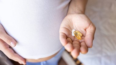 Doğum öncesi vitamin hapı. Mutlu gülümseyen kadın Omega 3 vitamini ile hap alıyor. D vitamini, E vitamini, Balık yağı kapsülleri