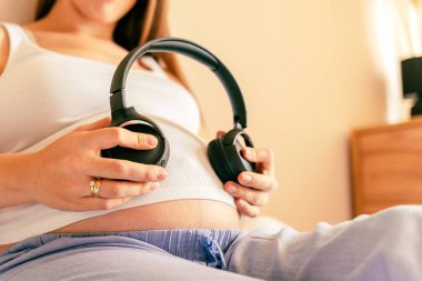 Hamile kadın müziği dinle. Neşeli hamile kız kulaklıkla müzik dinliyor. Anne göbek kulaklık sesi duyuyor. Hamilelik, ilaç sağlık hizmetleri ve insanların konsepti