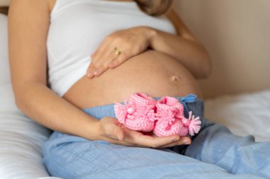 Hamilelik ayakkabıları. Pembe bebek ayakkabısı tutan mutlu hamile kadın. Küçük çocuk ayakkabısı. Hamilelik kavramı, annelik, bebek doğumu beklentisi