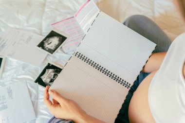 Hamile kadın yazma listesi. Genç hamile anne not defteri tutuyor. Hamile kadın bebek için kontrol listesi yazıyor. Gebelik kavramı, doğum