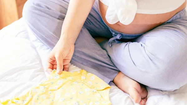 妊娠中のベビー服 黄色の赤ちゃんの服を着た美しい妊婦さん 妊娠中の女性は腹を抱え 妊婦病院の袋を詰める コンセプト妊産婦妊娠出産 — ストック写真