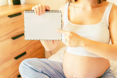 Hamile kadın yazma listesi. Genç hamile anne not defteri tutuyor. Hamile kadın bebek için kontrol listesi yazıyor. Gebelik kavramı, doğum