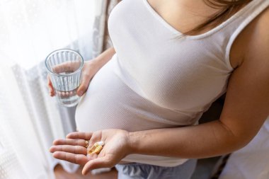 Pregnant woman pills vitamin. Happy smiling woman taking pill with supplement vitamin Omega 3. Vitamin D, E, A Fish Oil Capsules