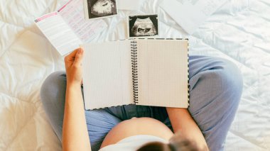 Hamilelik bebek listesi. Güzel hamile kadın kontrol listesi yazıyor. Elinde not defteri olan mutlu hamile kadın. Hamilelik, annelik, sağlık konsepti