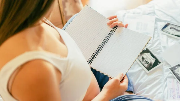 Pregnant writing baby list. Beautiful pregnancy woman writing check list. Happy pregnant lady holding notepad. Pregnancy, maternity, healthcare concept