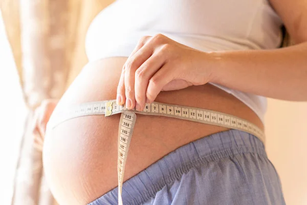 测量怀孕妇女的腹部 快乐的年轻孕妇带着测量腹部的带子 概念孕产 — 图库照片