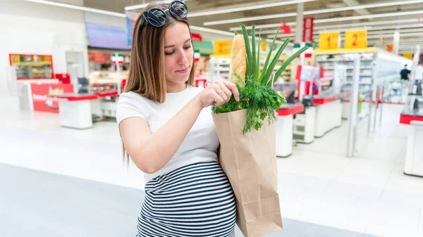 Pregnant food bag supermarket. Pregnancy woman with healthy lettuce salad leaves, fresh tomato in market food bag on grocery supermarket background. Everyday shopping concept
