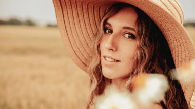 Buğday tarlası sahibi kadın. Güneş şapkalı mutlu genç kadın gün batımında buğday tarlasında. Doğa, yaz tatili, tarım ve insan konsepti