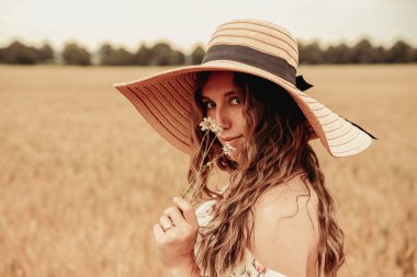 Kadın tarla buğdayı. Güneş şapkalı mutlu genç kadın gün batımında buğday tarlasında. Doğa, yaz tatili, tatil ve insanlar konsepti