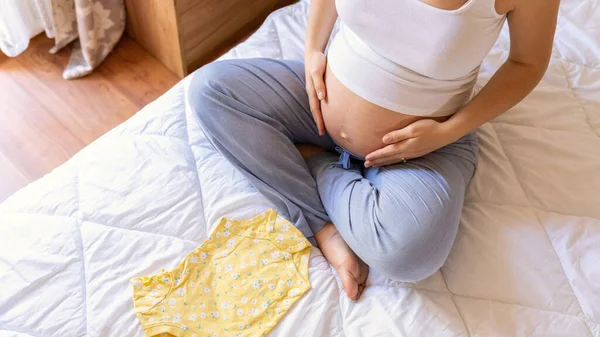 怀孕袋婴儿衣服 快乐的年轻孕妇抱着黄色的婴儿衣服 妈妈包装手提箱 为妇产医院的包 预期分娩的概念 — 图库照片
