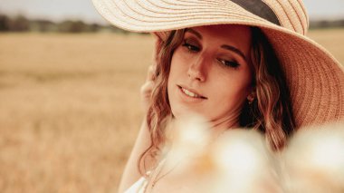 Kız buğday tarlası yazı. Güneş şapkalı mutlu genç kadın gün batımında buğday tarlasında. Doğa, yaz tatili, tatil ve insanlar konsepti